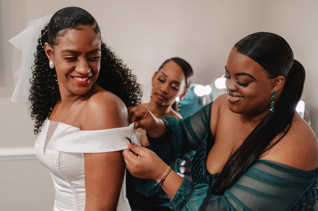 bride getting help during prep from her bridesmaids