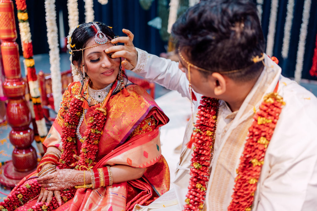 groom placing red dot on indian bride's forehead