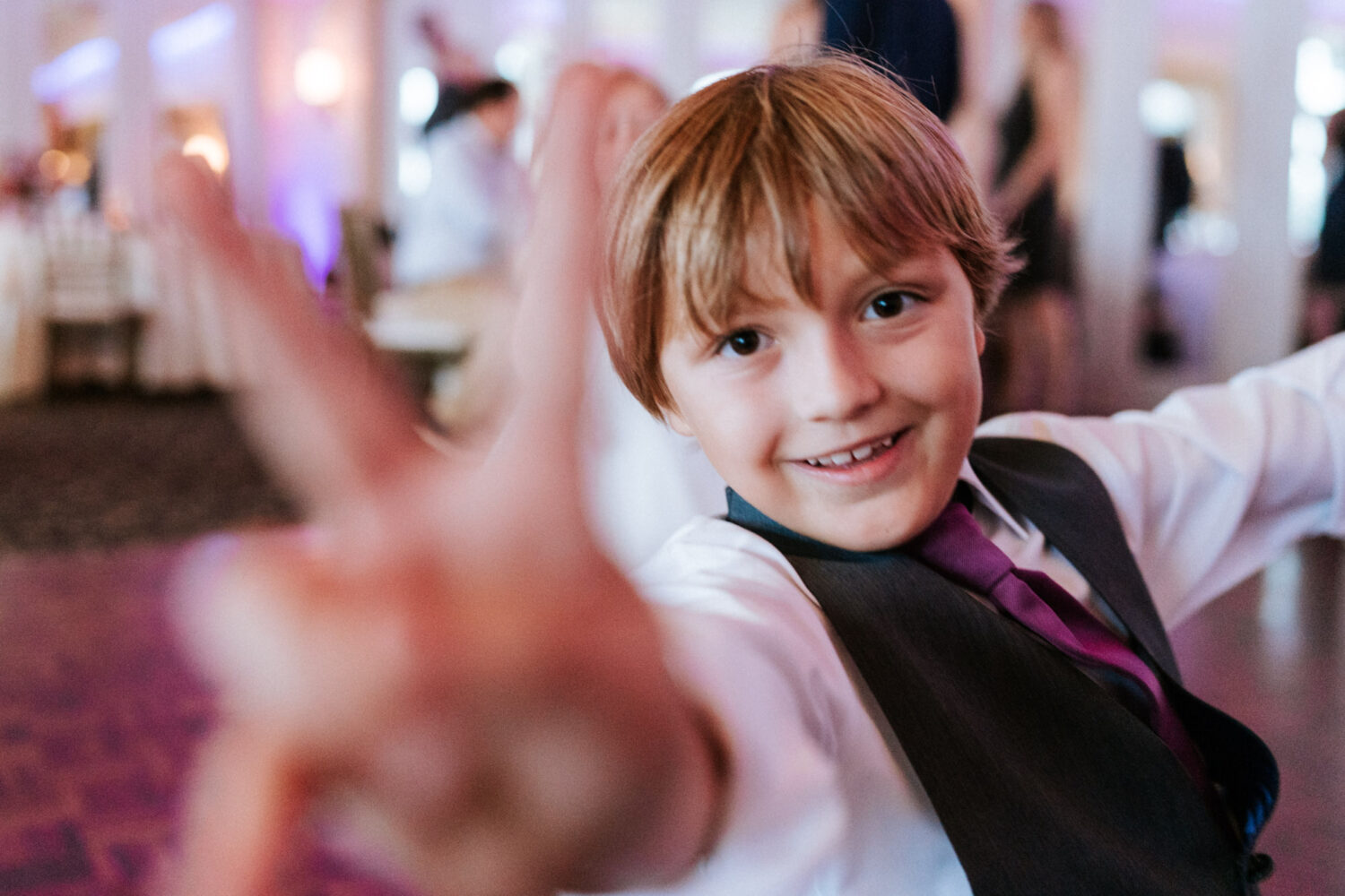 young boy dancing and waiving a peace hand sign to the camera during wedding reception