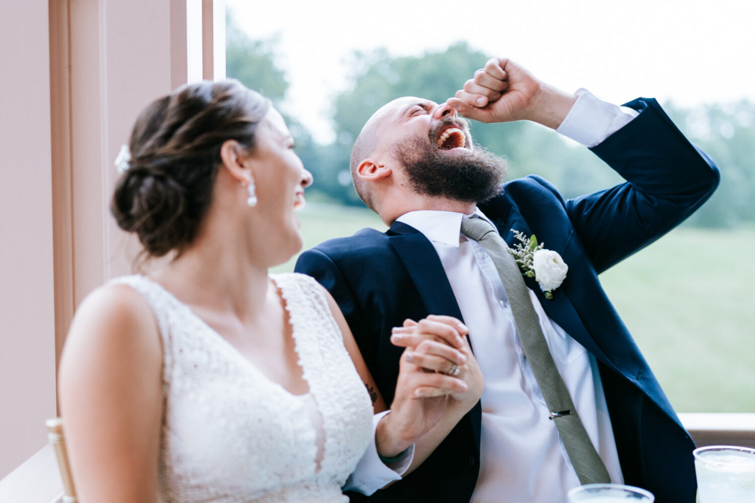 bride and groom laughing while listening to father of the bride give his wedding speech