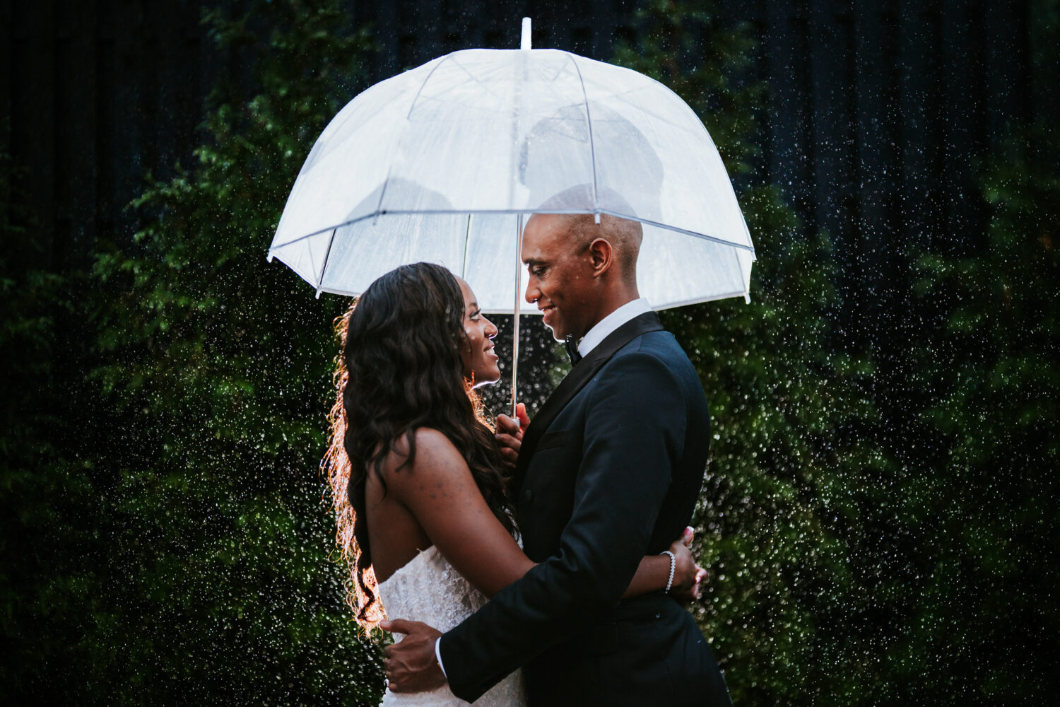 bride and groom hugging underneath an umbrella during portrait time in heavy rainfaill
