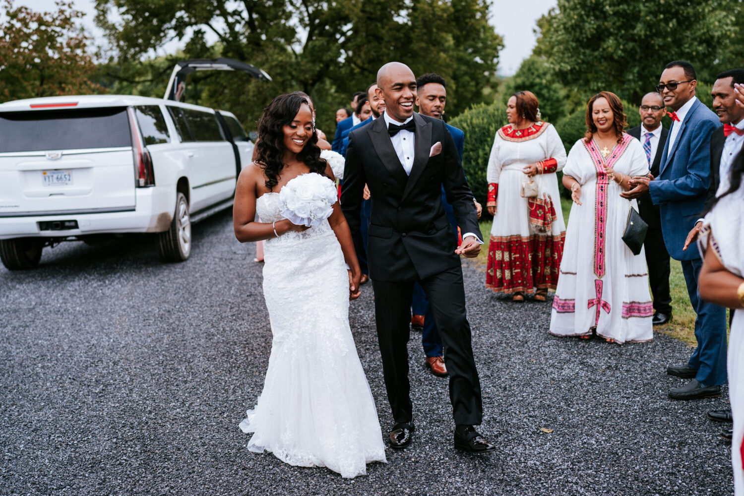 bride and groom walking together on their wedding day with family watching