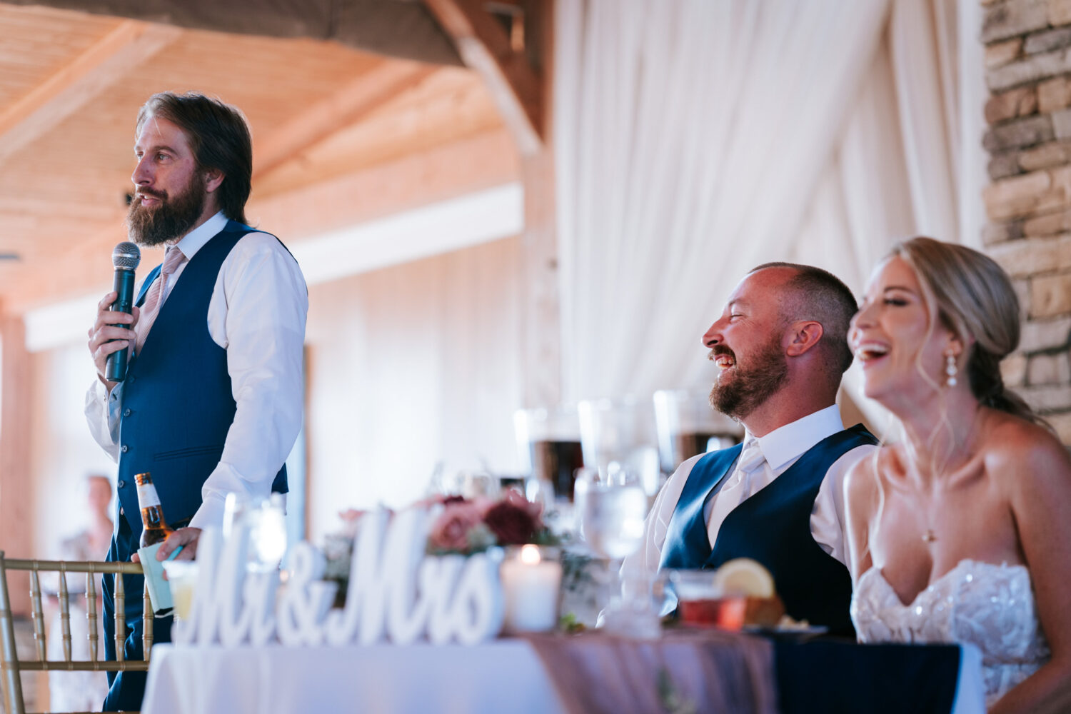 bride and groom laughing together while the best man gives his wedding speech
