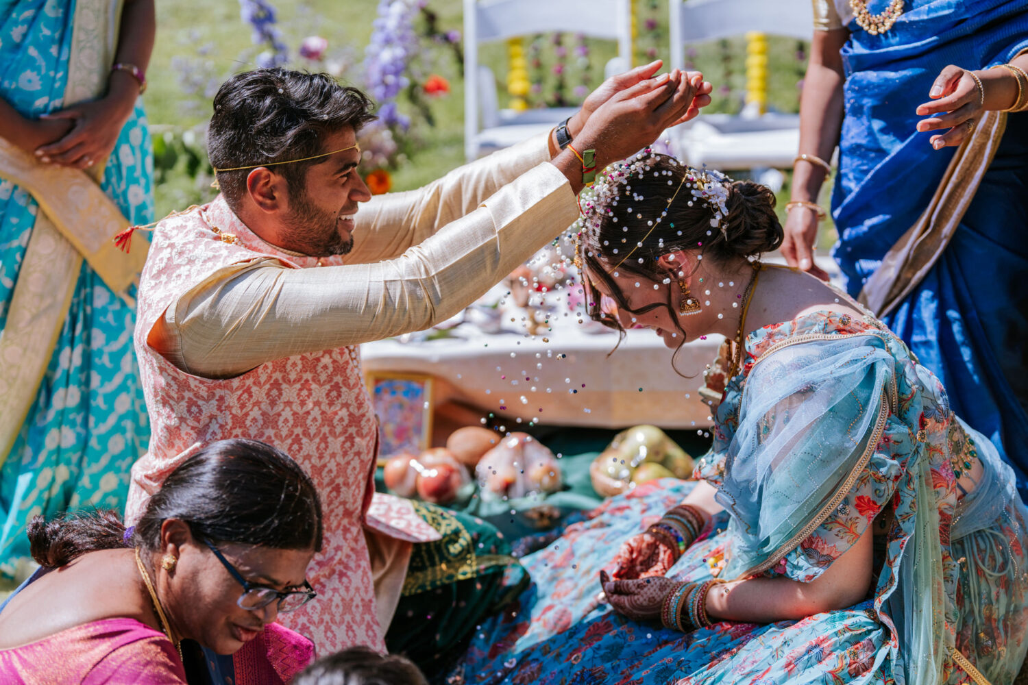groom pouring beads onto brides head during indian wedding ceremony