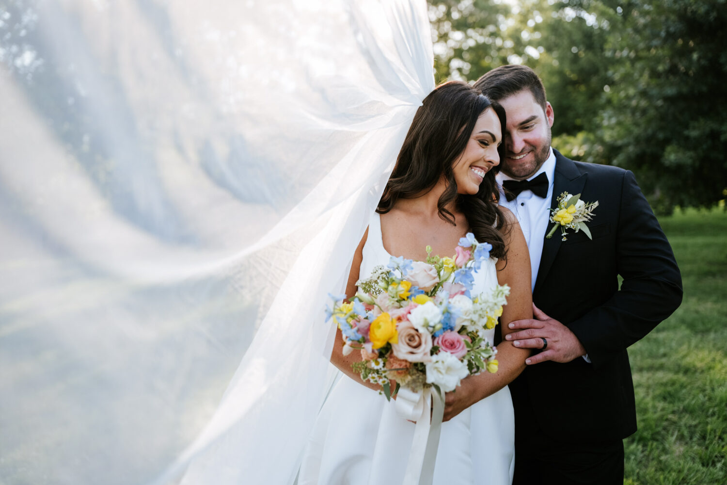 bride and groom smiling with each other with the bride's veil floating