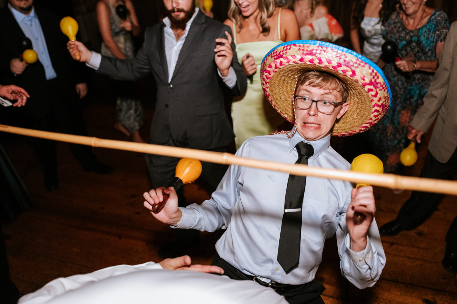 wedding guest trying to get underneath a limbo stick while wearing a sombrero