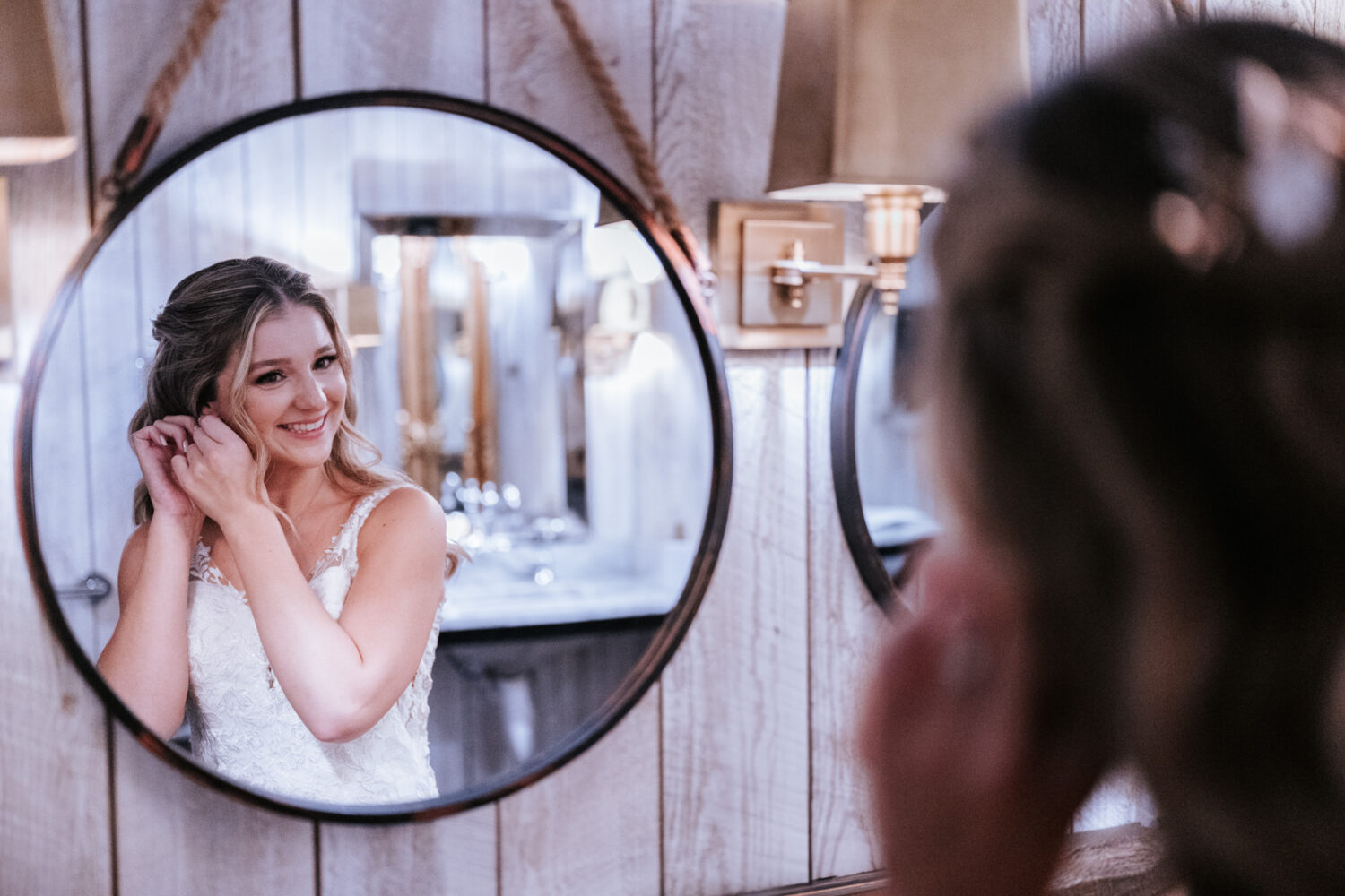 bride fixing her earring while looking into a mirror on her Sweeney Barn wedding day