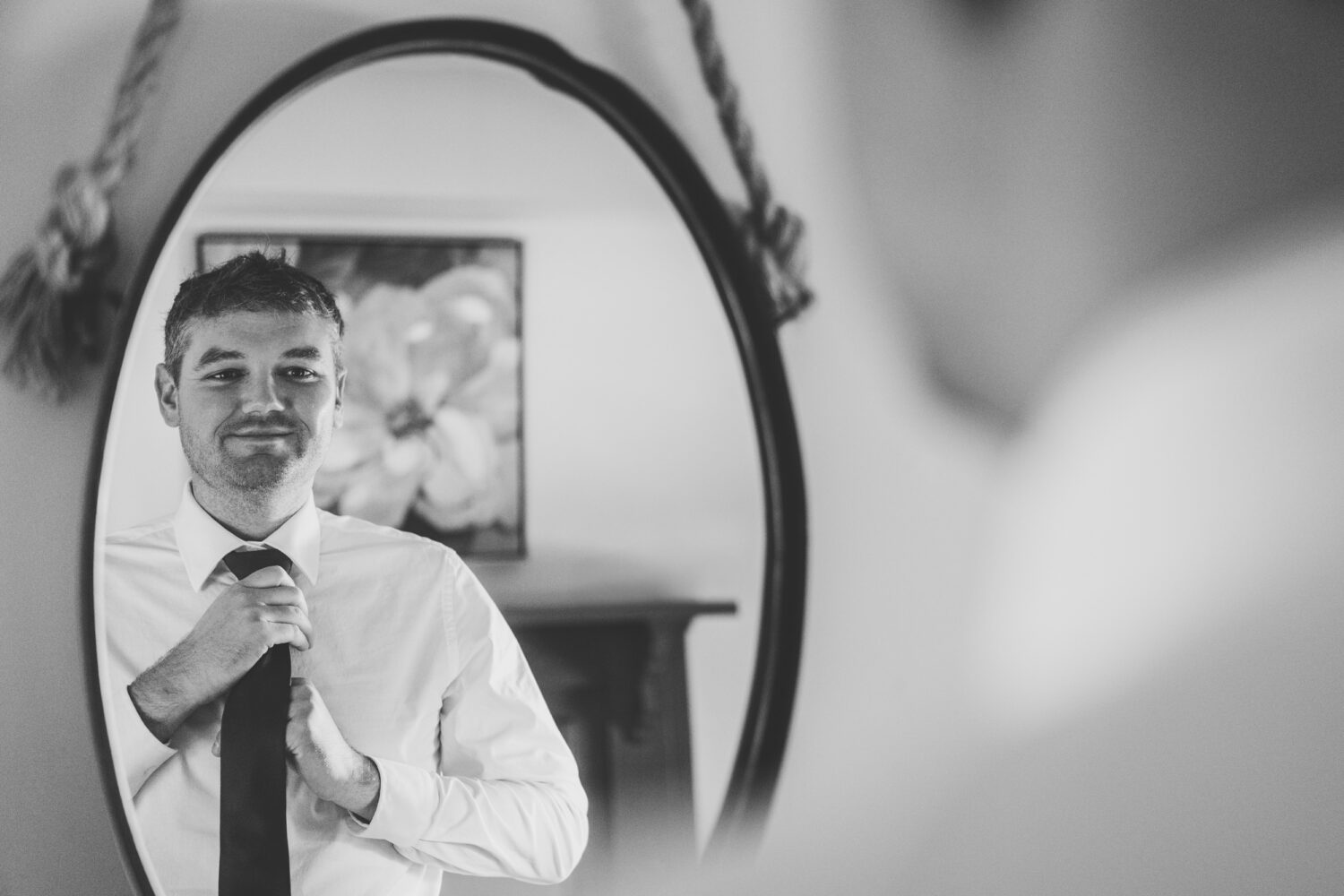 groom tying his tie while looking into the mirror on his wedding day