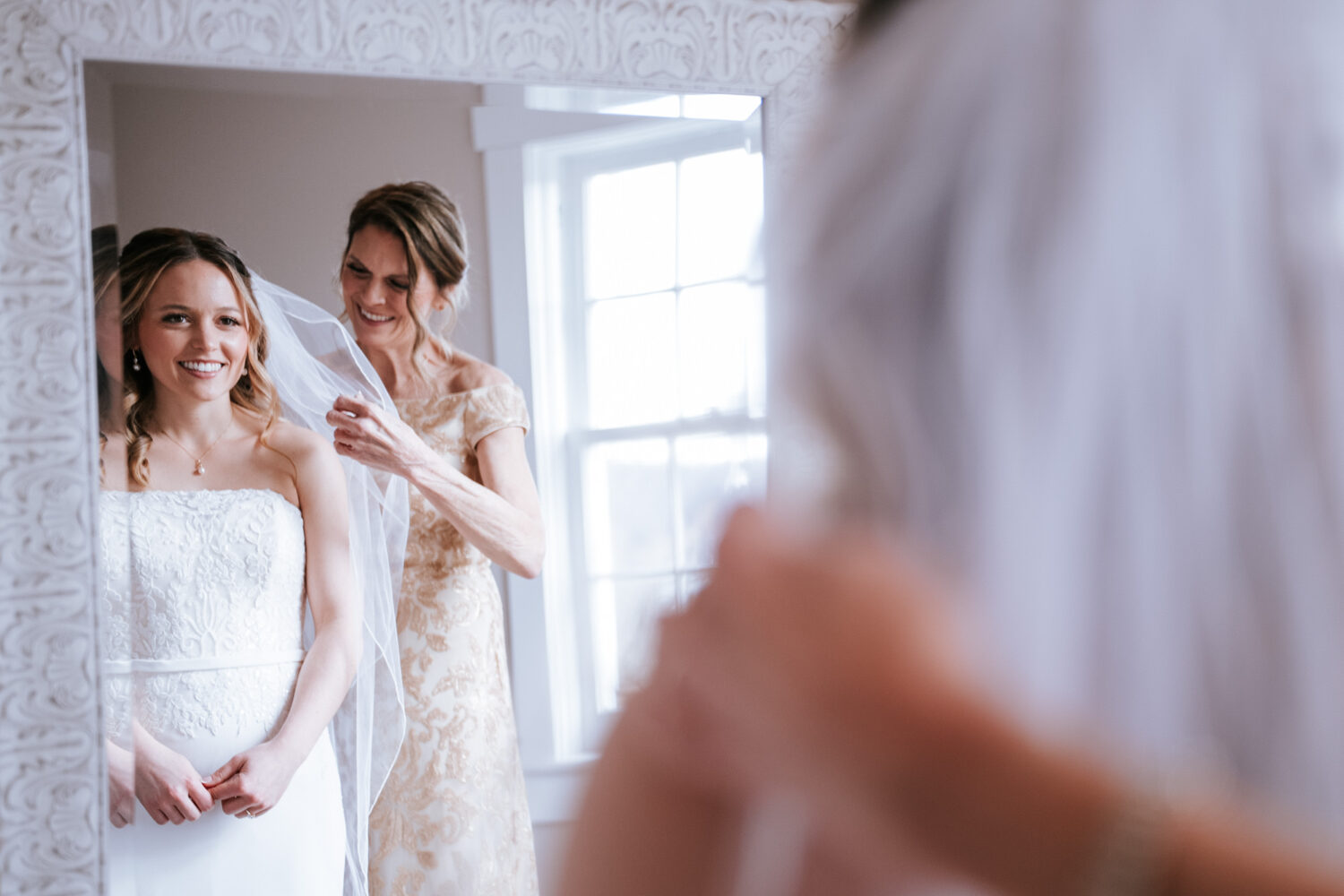 bride looking into the mirror and smiling as her mother adjusts her veil