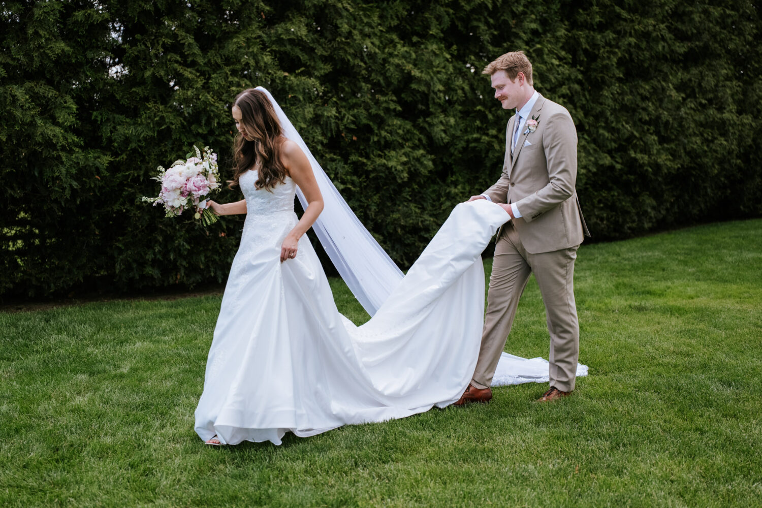 groom holding his bride's dress while they walk away together
