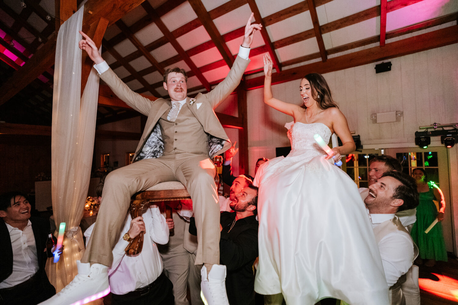 bride and groom being lifted in the air by their wedding guests while sitting on chairs during their shadow creek wedding reception