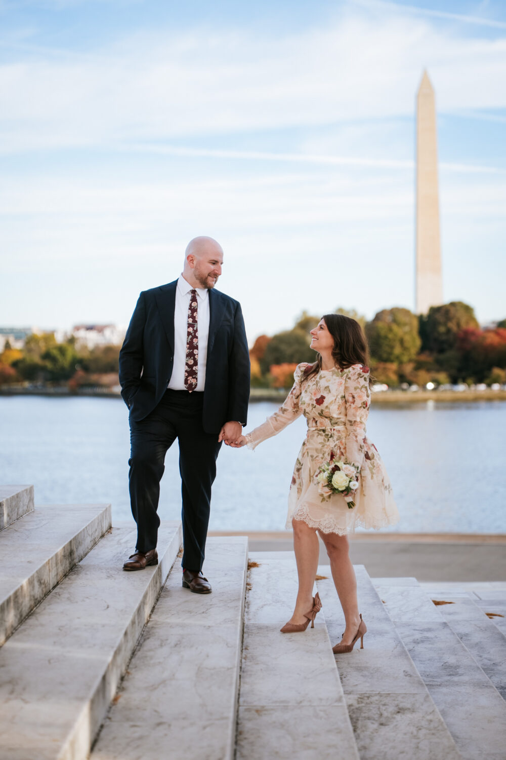 Engaged couple walking up Jefferson Memorial steps with the Washington Monument in the background