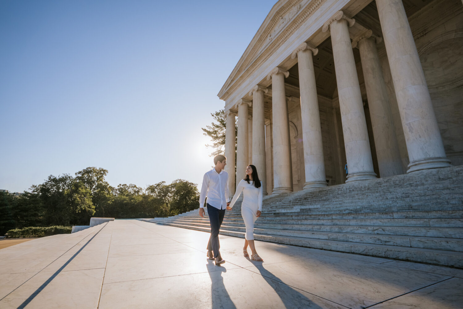 Engaged couple walking hand in hand outside the Jefferson Memorial during golden hour engagement session