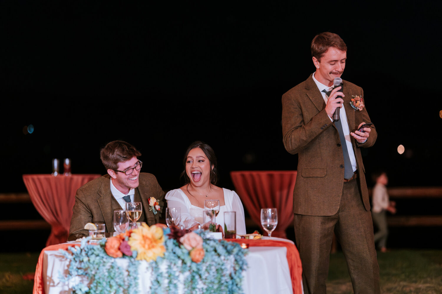 Couple laughing during a hilarious wedding toast under the stars

