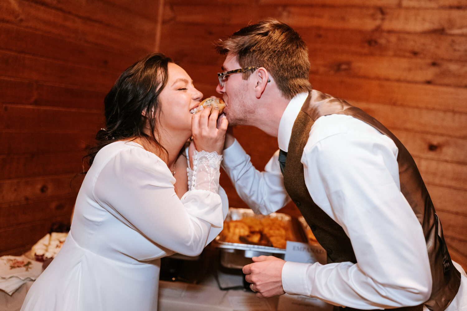 Bride and groom take a bite of an empanada together at the reception
