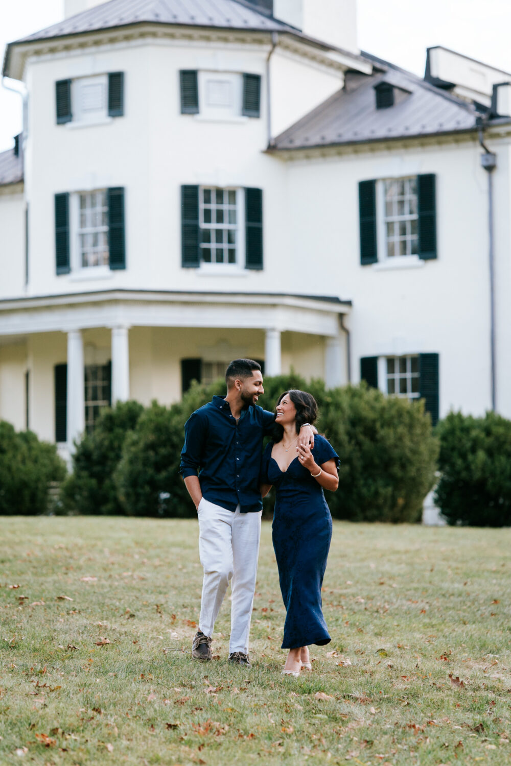 Newly engaged couple walking and laughing in front of a historic white house