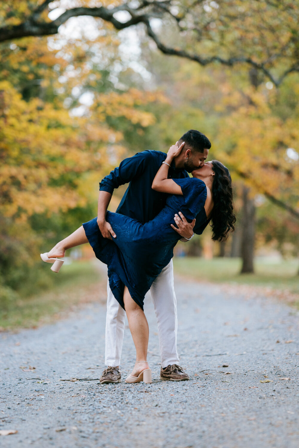 Fiancé lifting his bride-to-be for a kiss on a tree-lined gravel path
