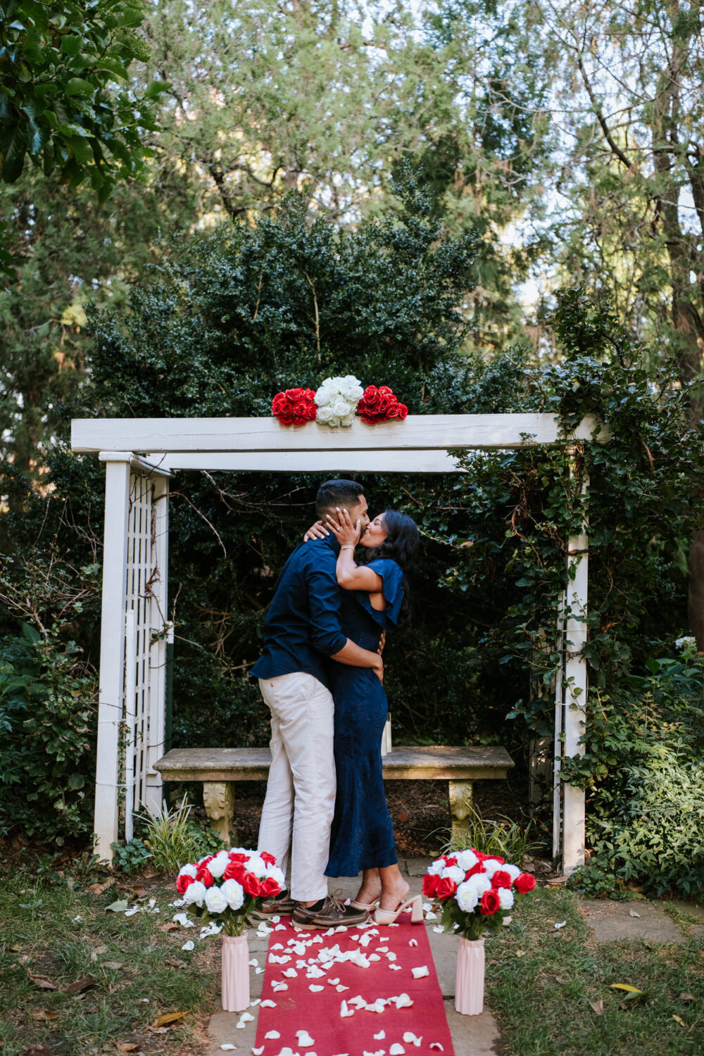 Couple shares a kiss after a surprise proposal at a romantic garden setup in Leesburg, Virginia.