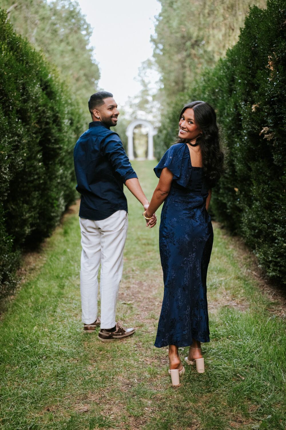 Couple holding hands and walking through the garden after their surprise proposal at Oatlands Historic House & Gardens in Leesburg, VA.