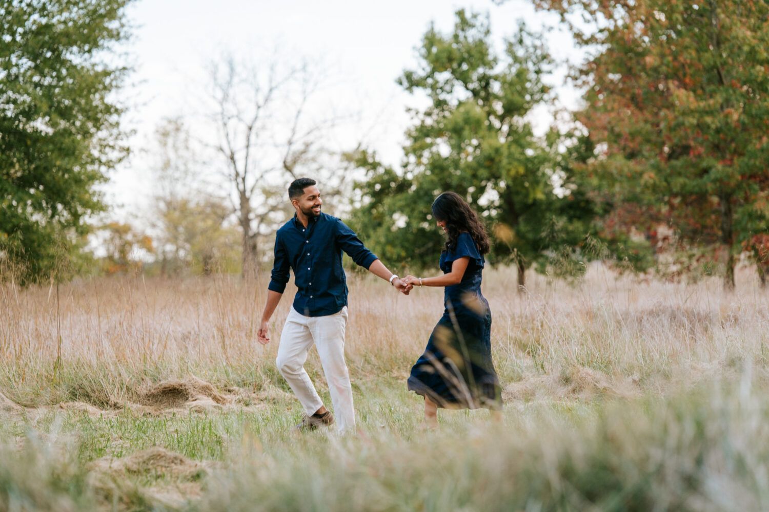 Couple walking hand in hand through tall grass after their surprise proposal