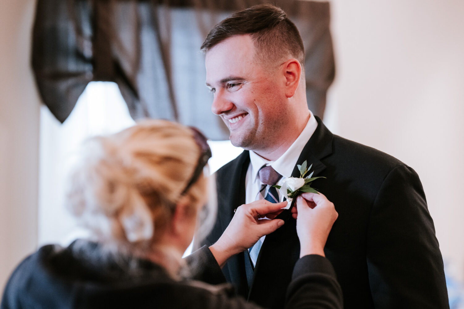 Groom smiling while getting boutonniere pinned before his Rosemont Springs wedding ceremony
