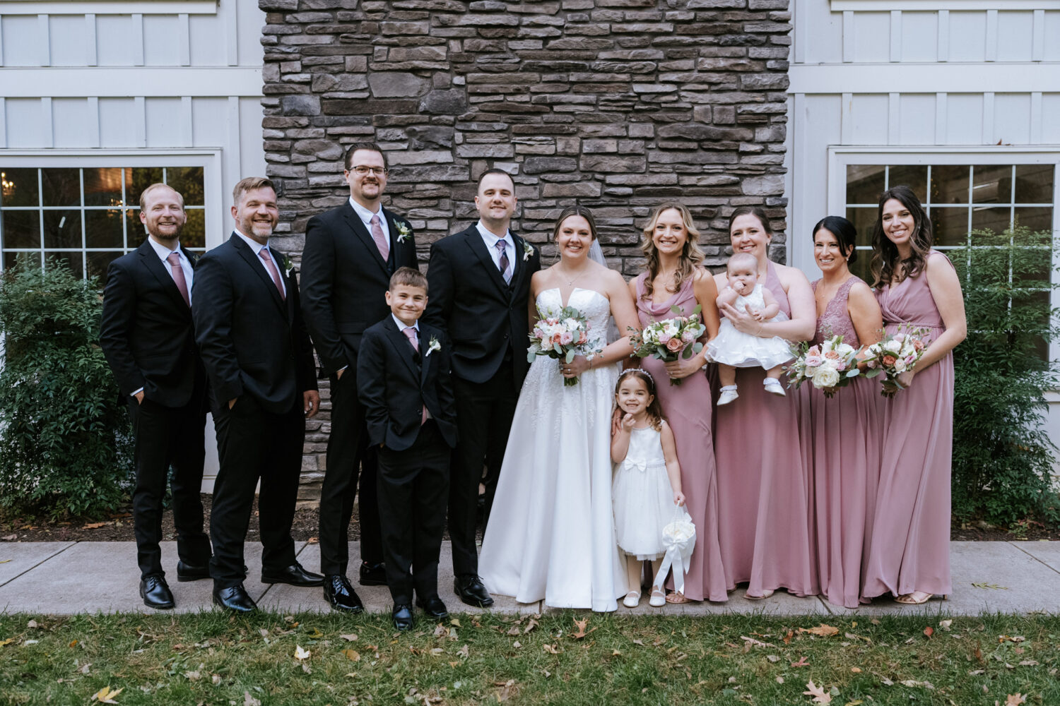 Wedding party portrait with bride, groom, and family in front of stone wall at Rosemont Springs
