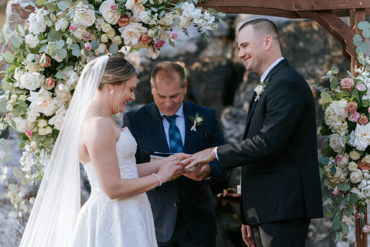 Bride and groom exchanging rings under floral arch at Rosemont Springs ceremony

