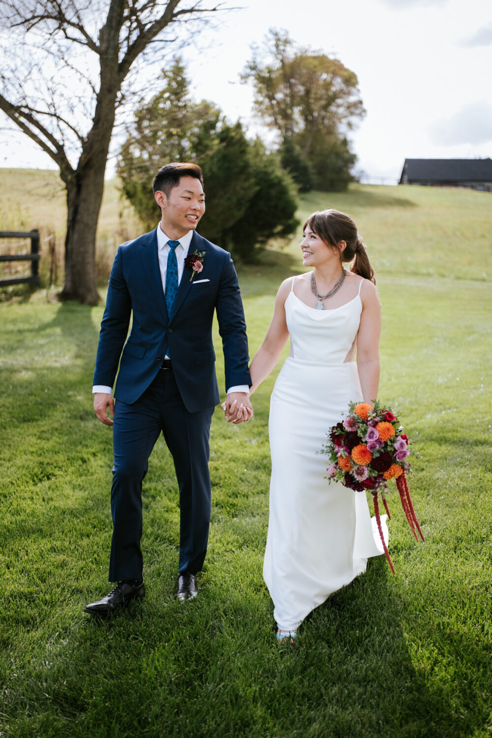 Couple walking hand in hand through a grassy field at their fall wedding
