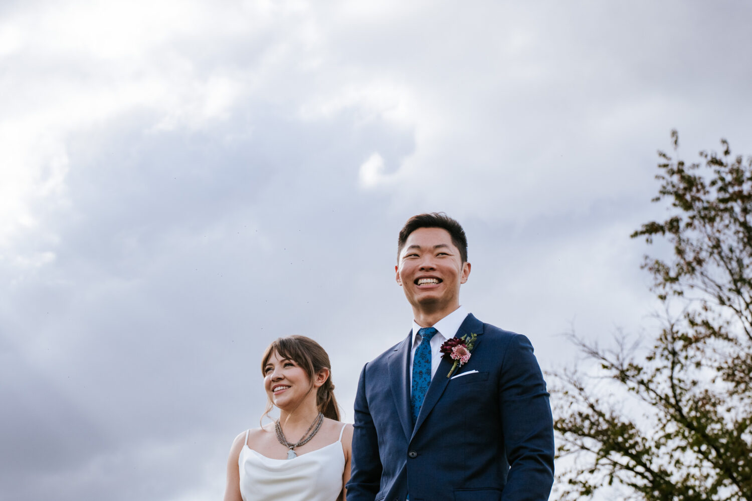 Smiling bride and groom enjoying a candid moment under a cloudy sky
