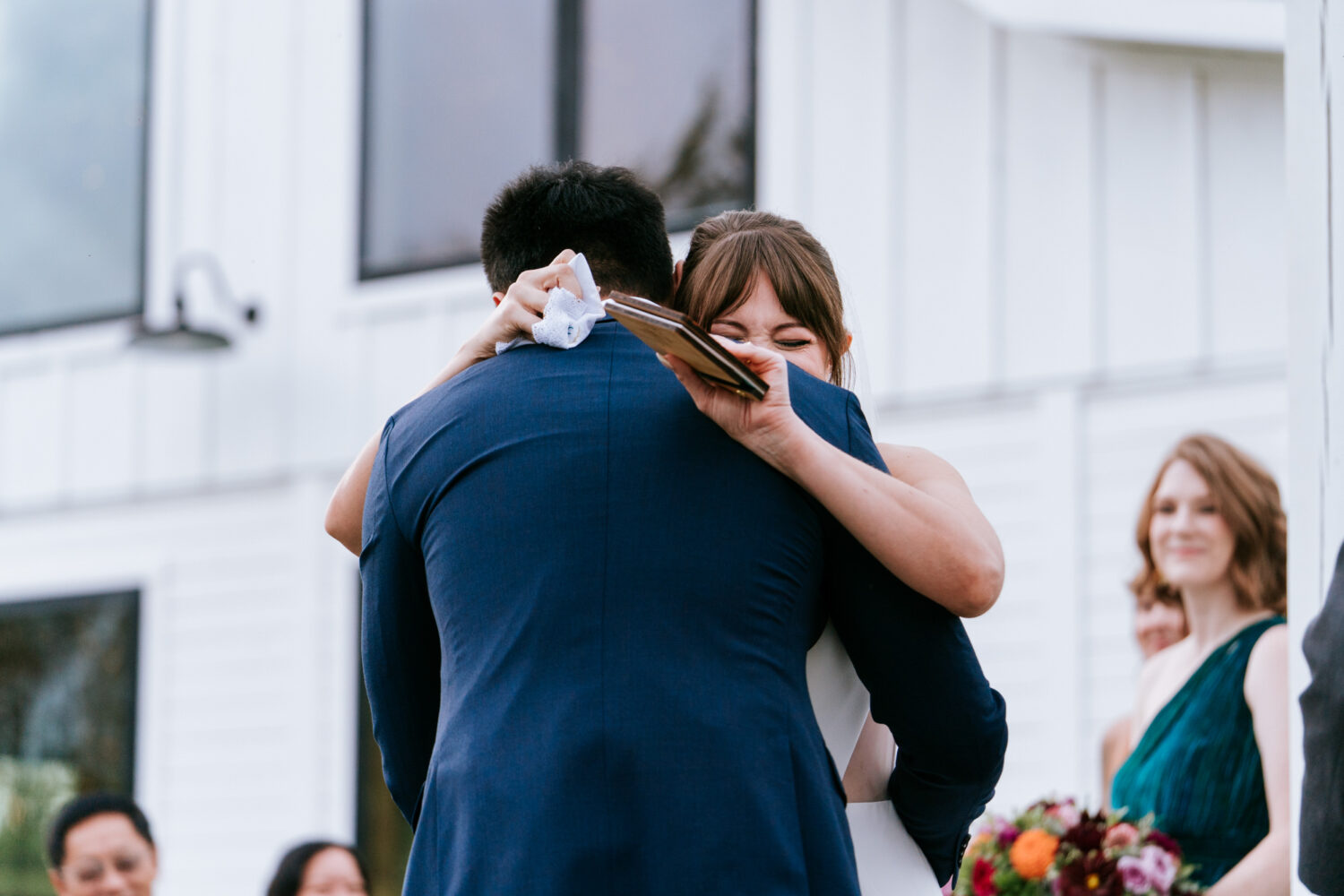 Bride hugging groom tightly with vows in hand during emotional ceremony moment
