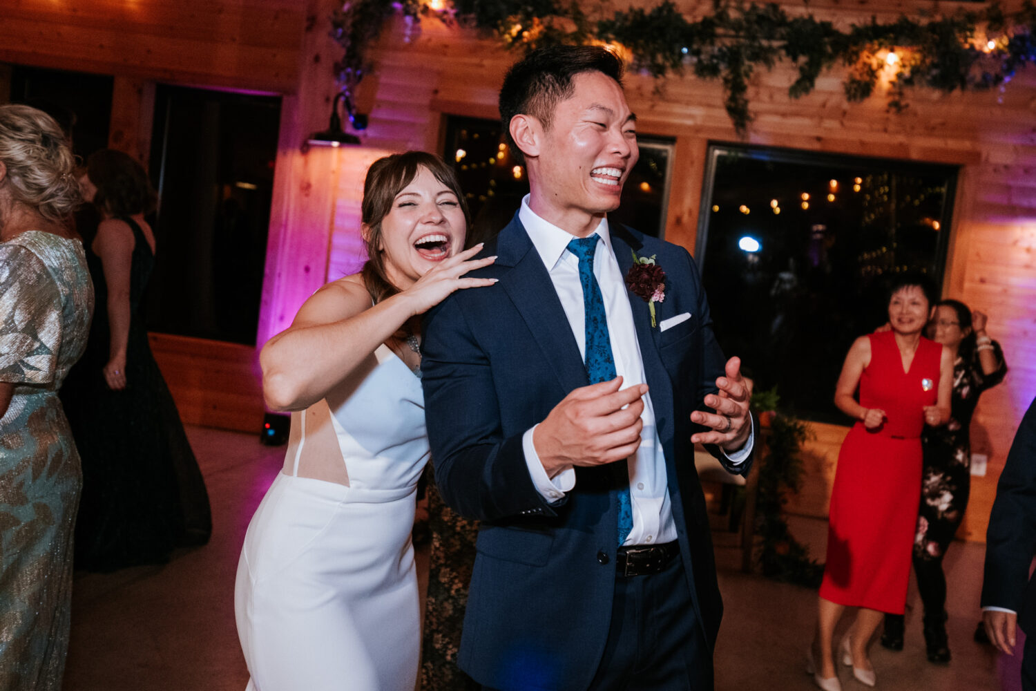 Couple laughing together on the dance floor surrounded by guests
