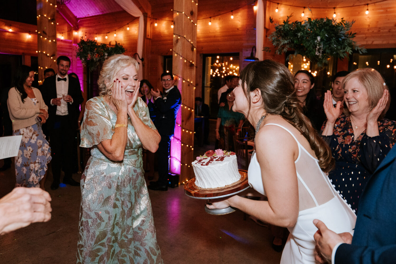 Bride surprising her mother with a cake during joyful reception moment

