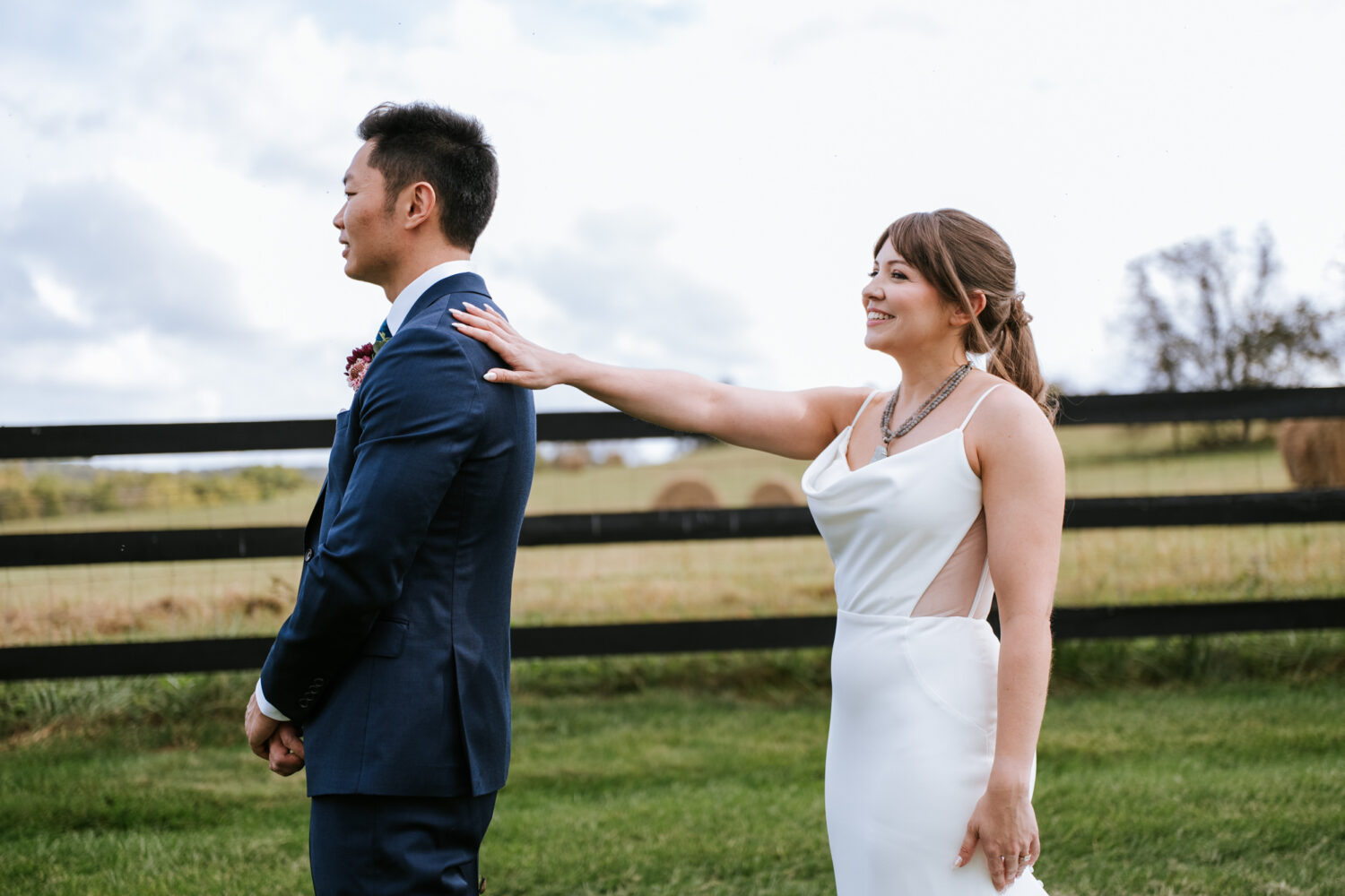 Bride tapping groom’s shoulder for emotional first look moment outdoors
