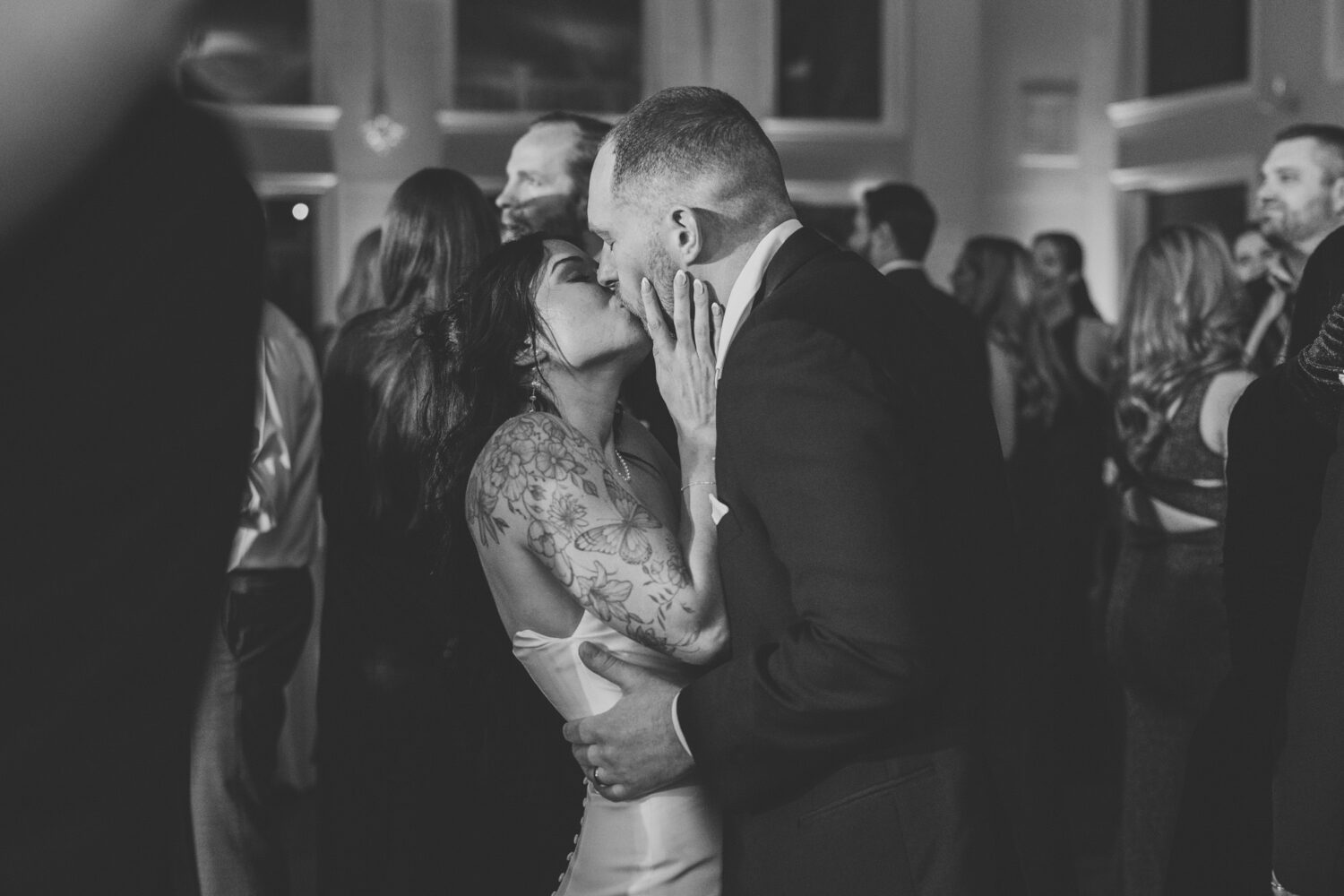 Bride and groom kissing on crowded dance floor wedding reception