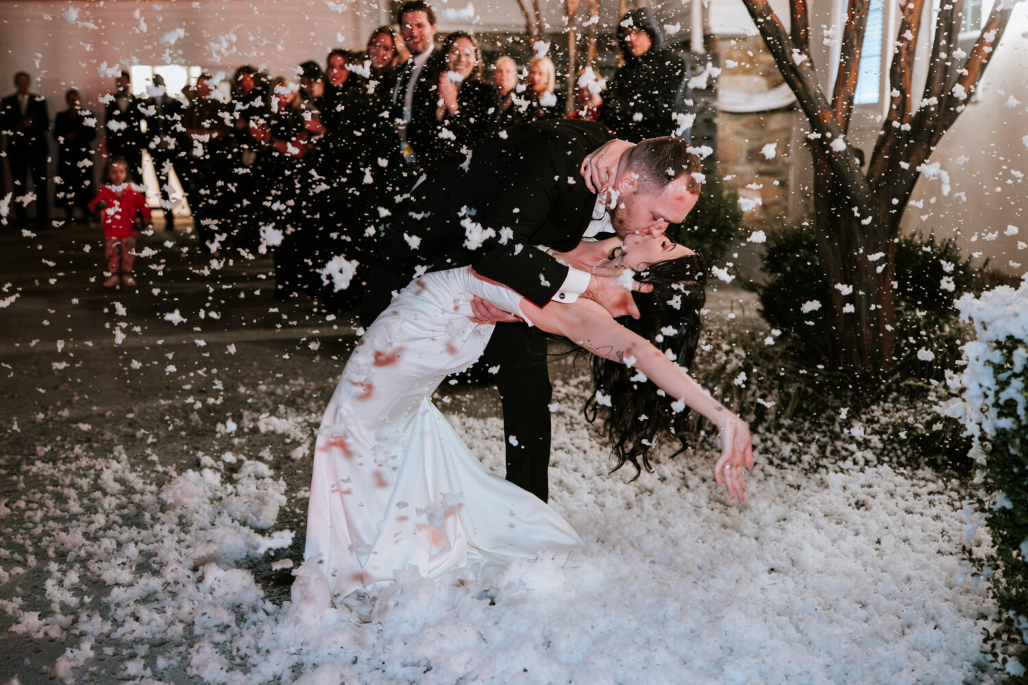 Bride and groom dip kiss during snowy wedding exit